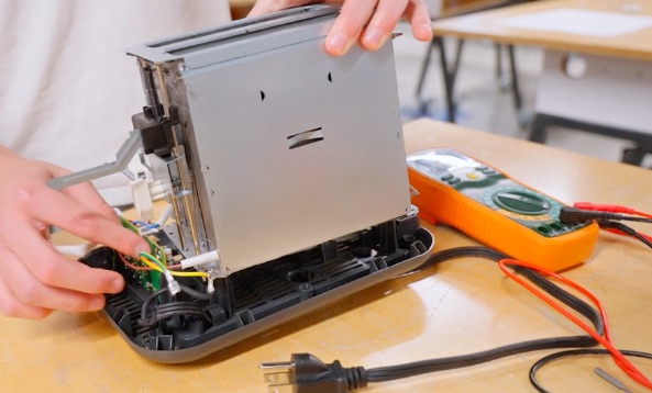 A toaster opened up on the bench next to a multimeter